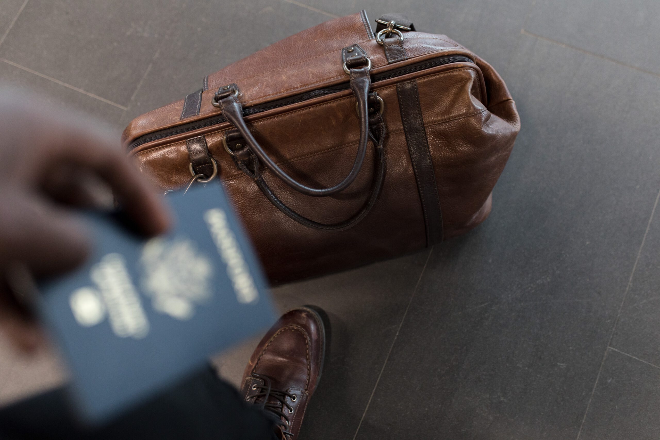 Mężczyzna trzymający w rece paszport i stojący nad skórzaną brązową torbę podróżną