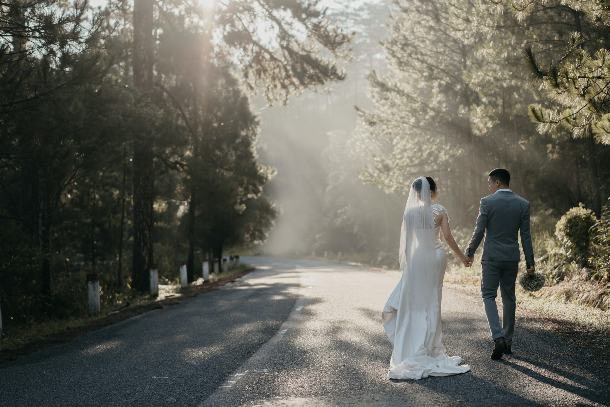 Para młoda w ślubnym stroju na spacerze asfaltową drogą w lesie