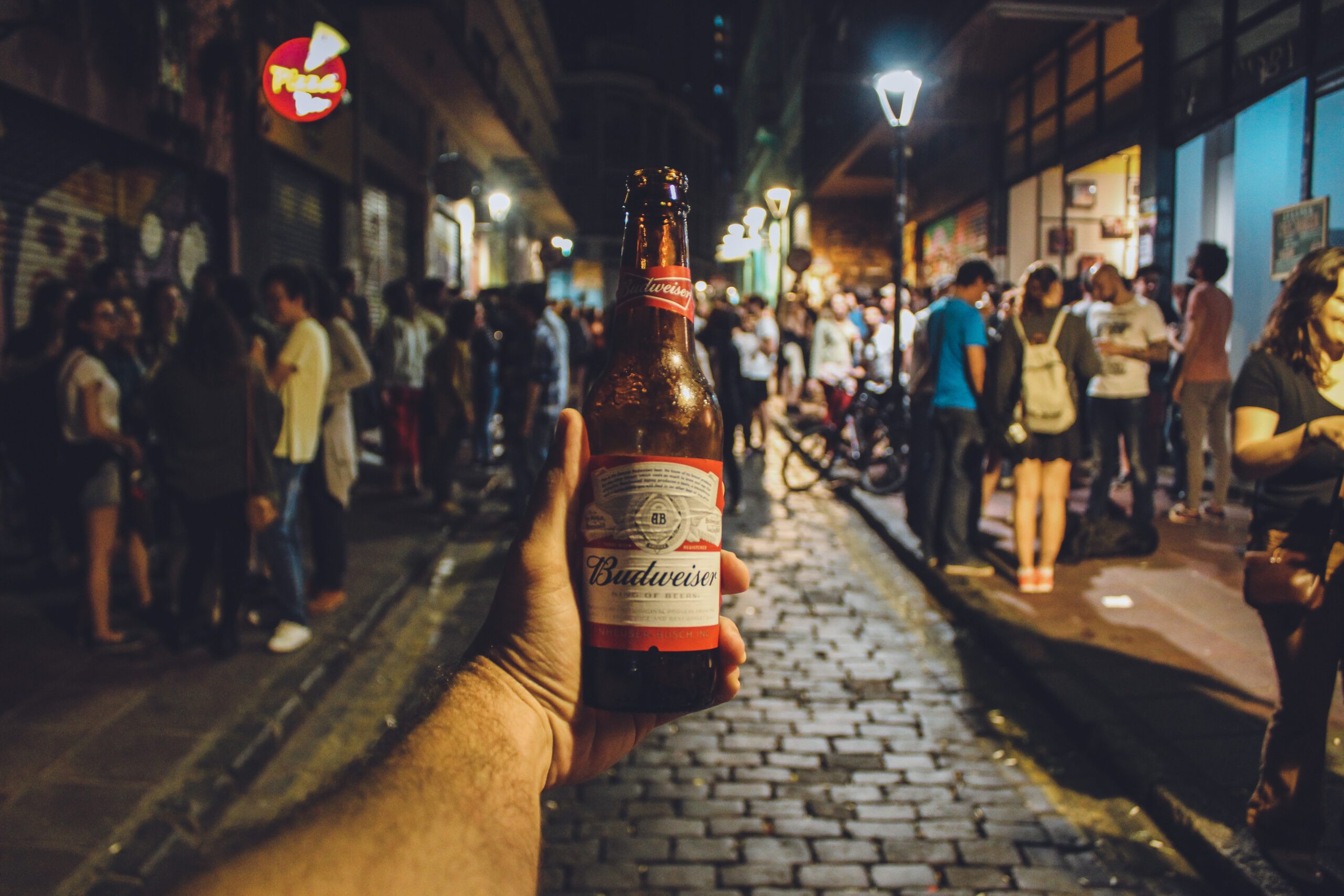 Piwo butelkowe trzymane przez kogoś w ręce na tle ludzi zgromadzonych na ulicy przy strefie kibica